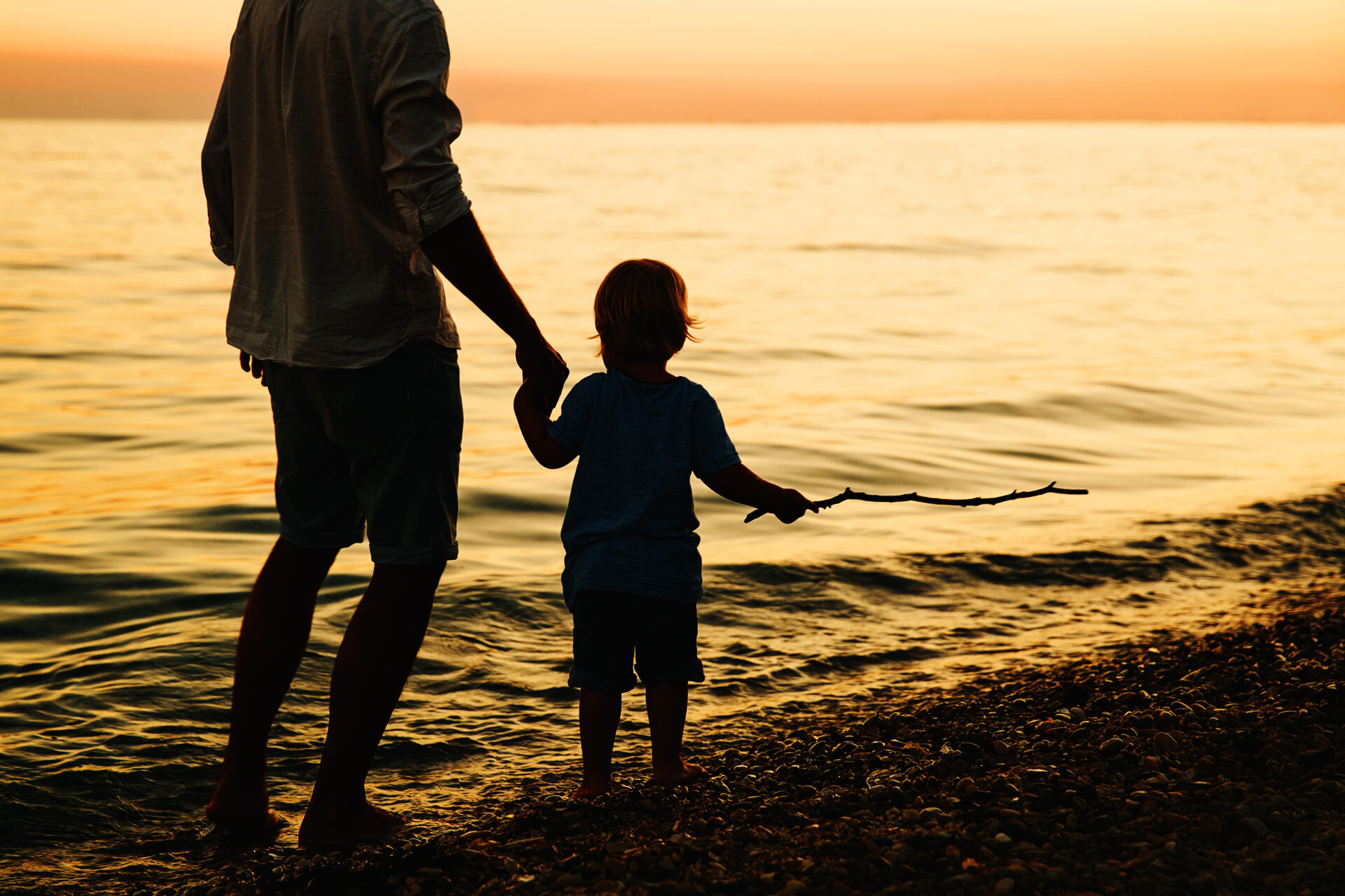 Father and son back silhouettes walking by the sea